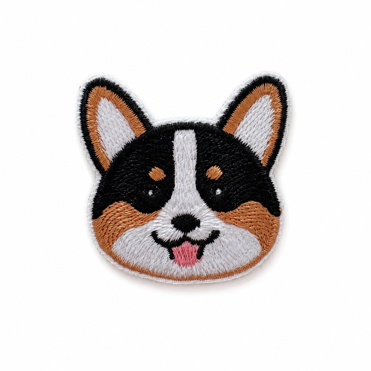 An embroidered patch shaped like a corgi dog face, featuring black, white, and tan fur with a small pink tongue, shown on a plain white background.