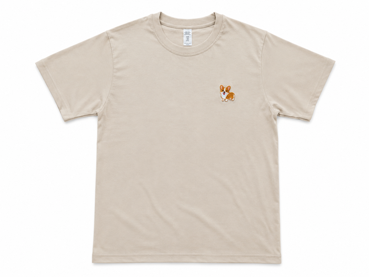 A light beige crewneck t-shirt with a small embroidered dog graphic on the left chest, displayed flat against a white background.