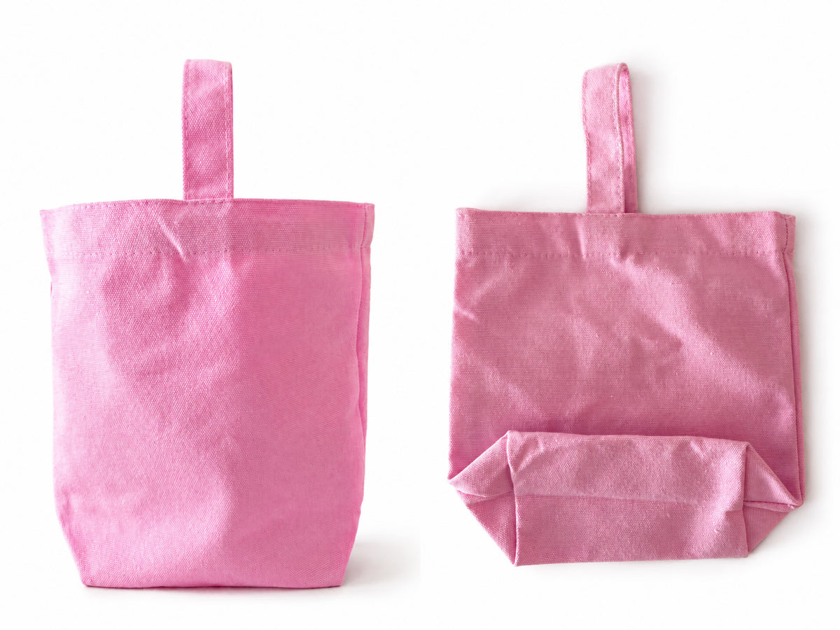Two view of pink fabric tote bags with top handles, shown side by side on a plain white background. The bag on the left is open and standing upright, while the bag on the right is folded with the bottom flap folded up.